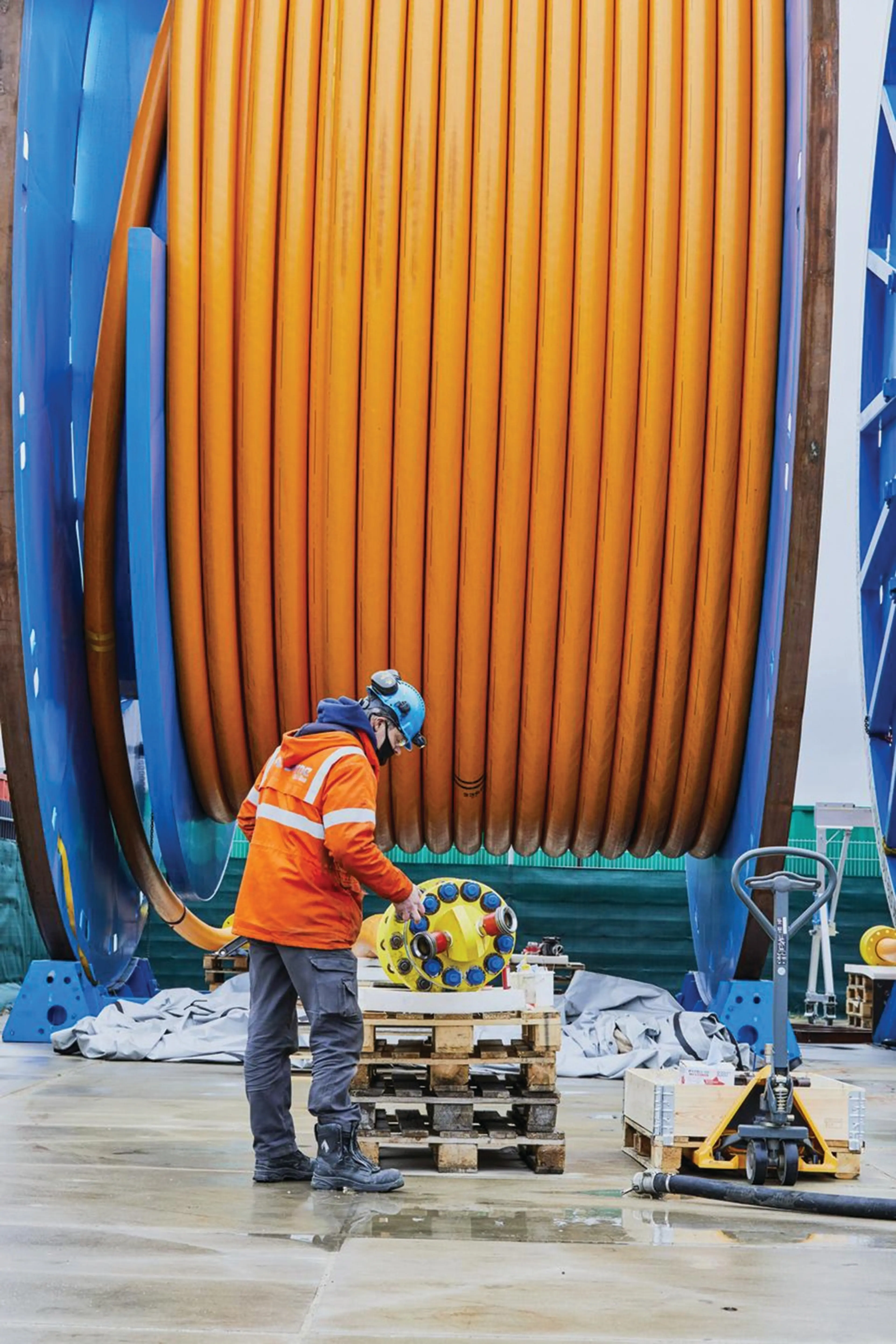 A man wearing an orange jacket is working in front of large reel cable.