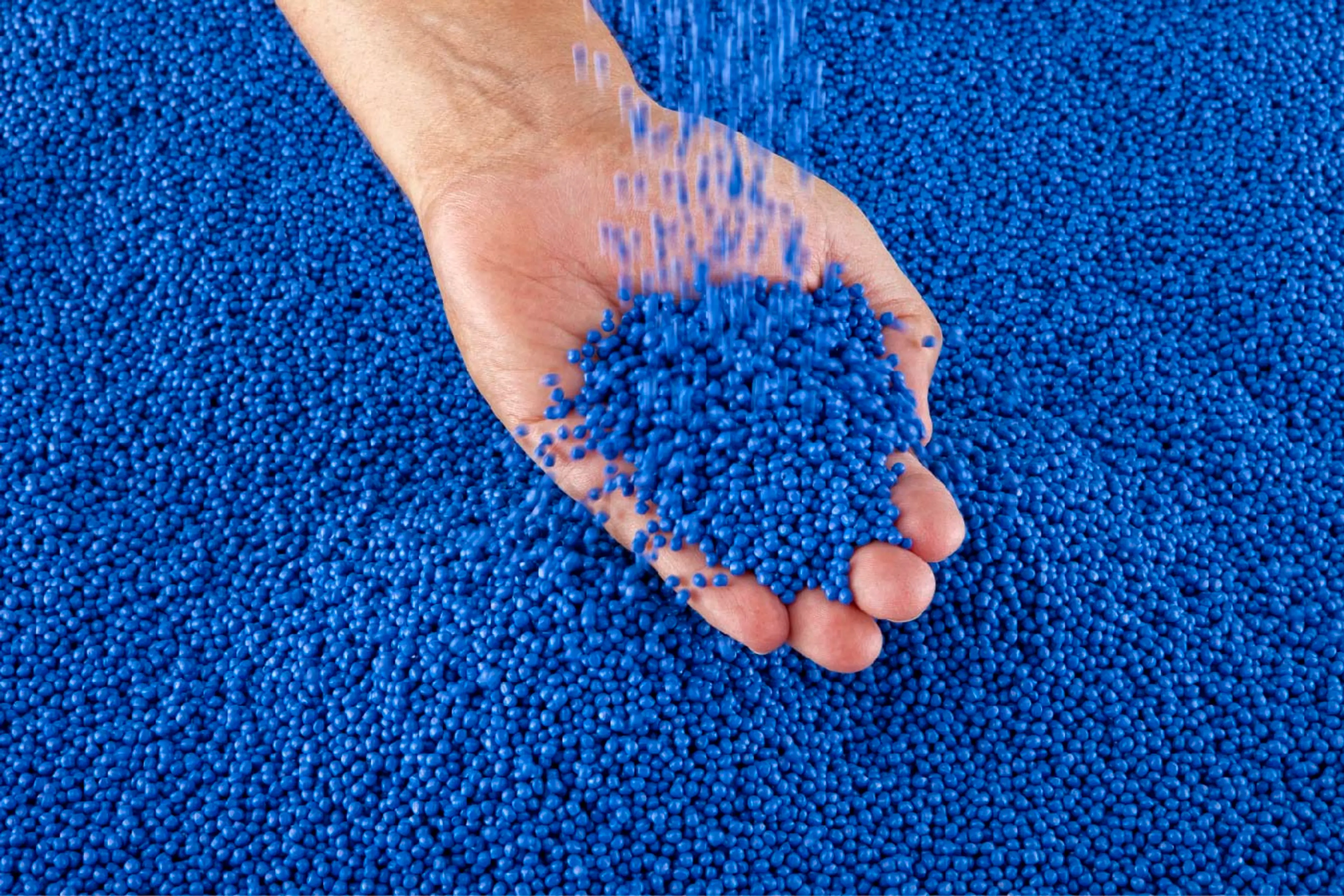 Hand in bucket of blue plastic pellets