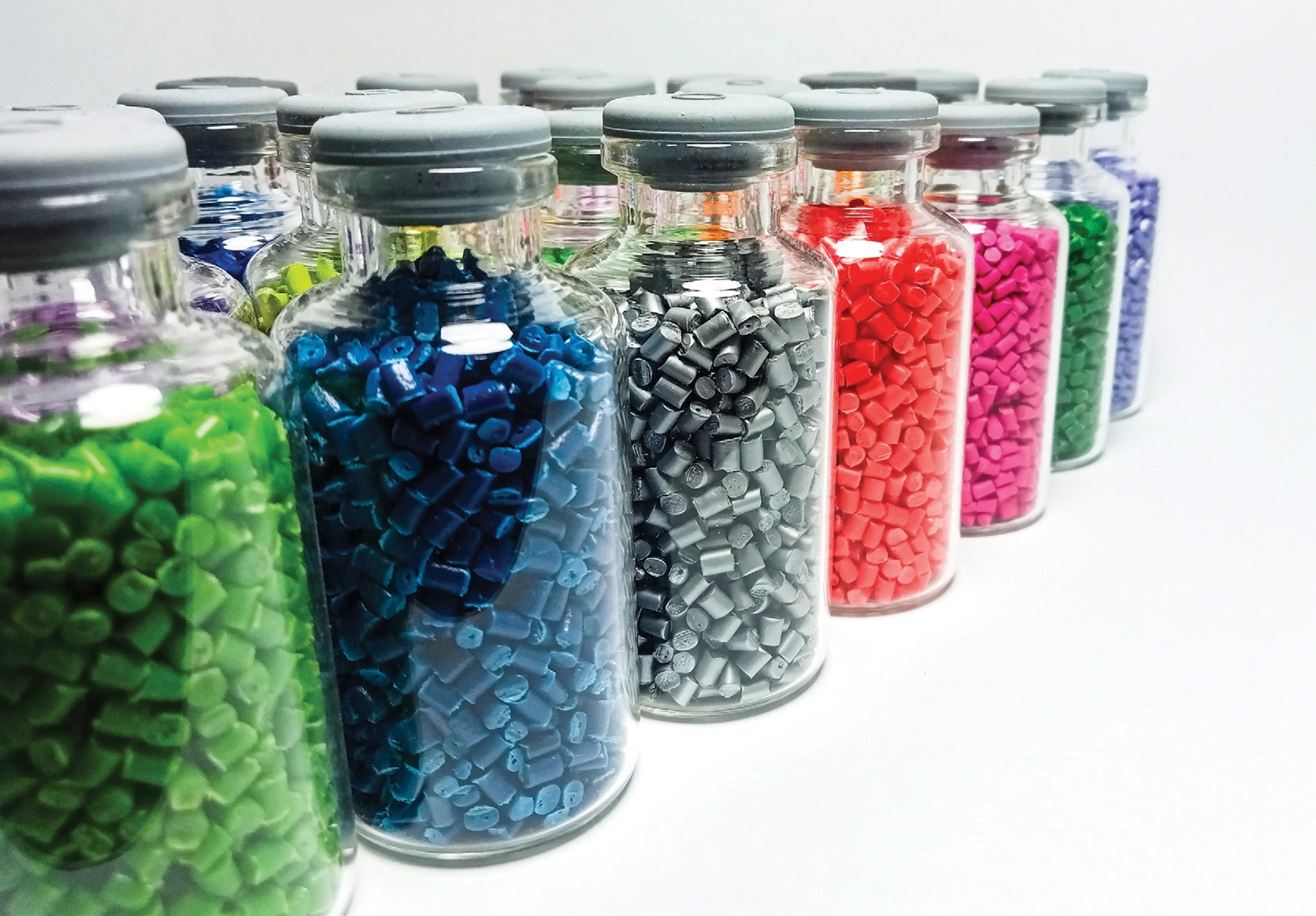 Glass jars of colourful plastic pellets on white background