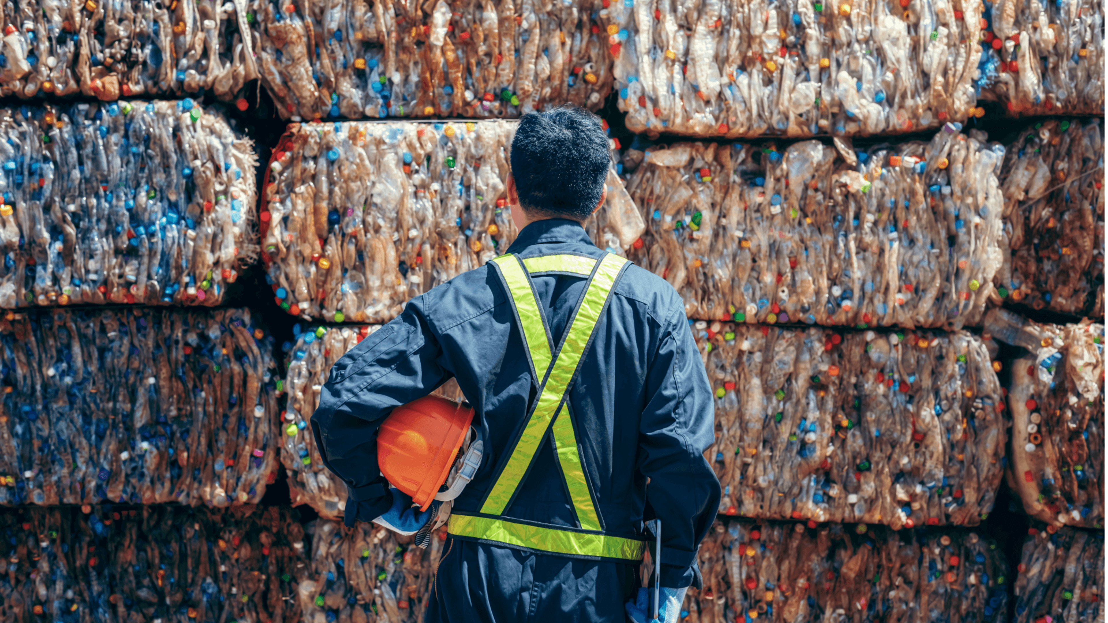 Man holding hard hat staring at large bales of recycling plastics bottles